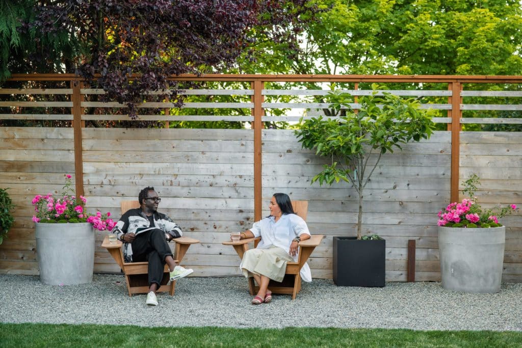 Bobby and Edith sitting in the adirondack chairs on gravel area surrounded by container plants.