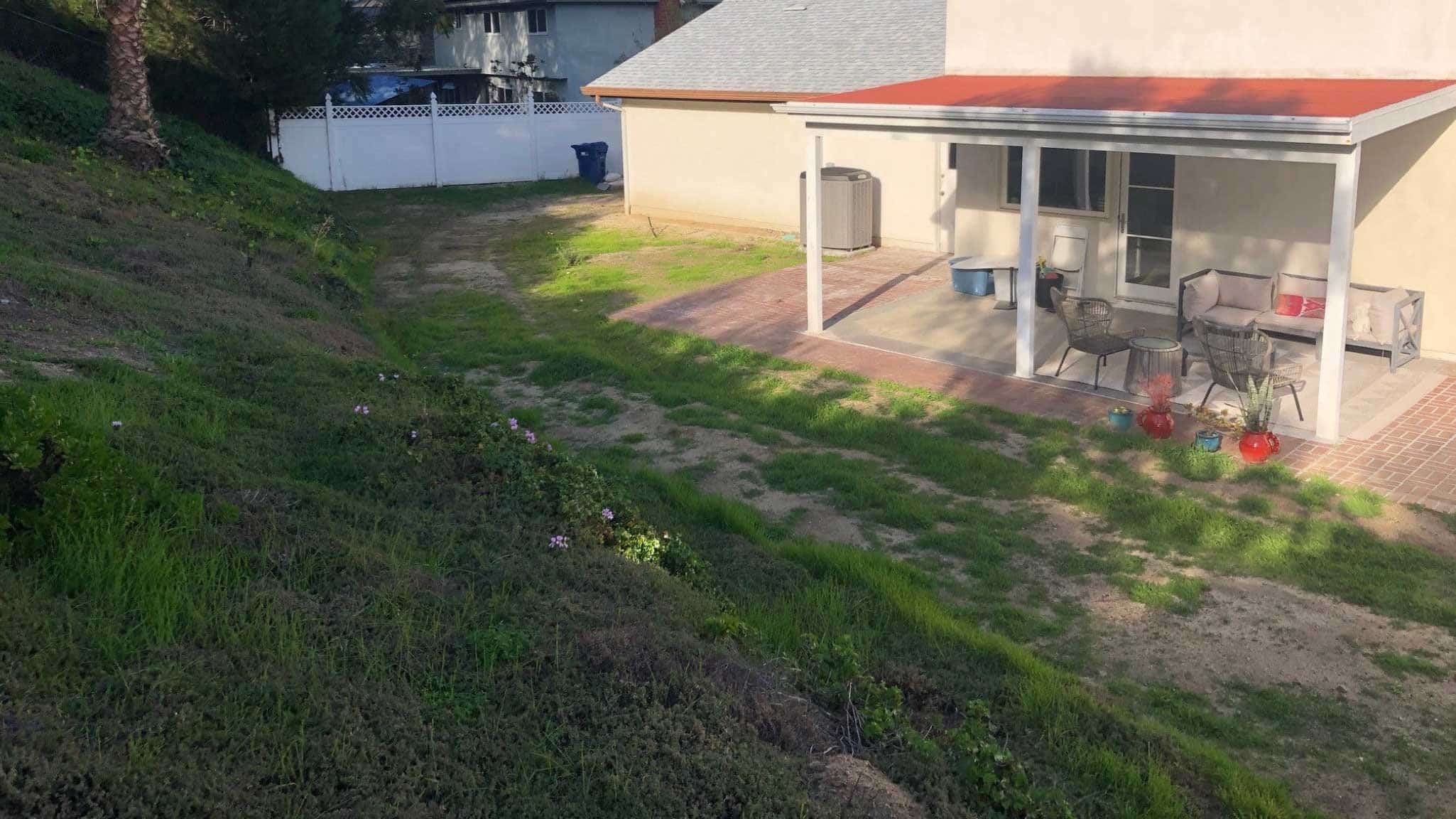 Before photo of yard taken from back slope toward home with patchy grass and dated patio